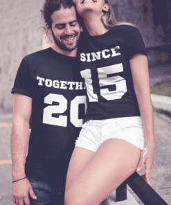 Happy couple wearing matching graphic T-shirts with years and messages, celebrating together.