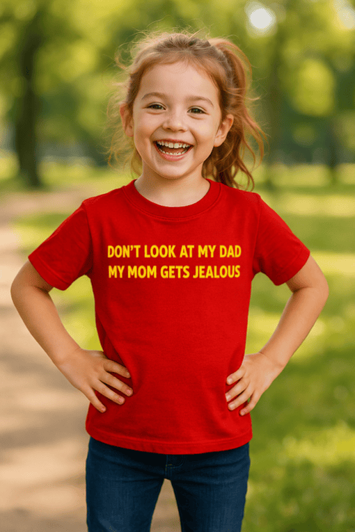 Happy kid wearing red funny T-shirt with humorous message about family jealousy outdoors.