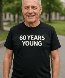Older man wearing a humorous black t-shirt that says "60 YEARS YOUNG" outdoor in park, celebrating milestone.