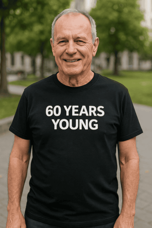 Older man wearing a humorous black t-shirt that says "60 YEARS YOUNG" outdoor in park, celebrating milestone.