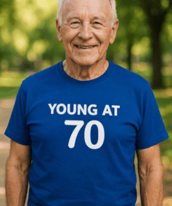 1. Older man smiling wearing a "Young at 70" birthday t-shirt outdoors.