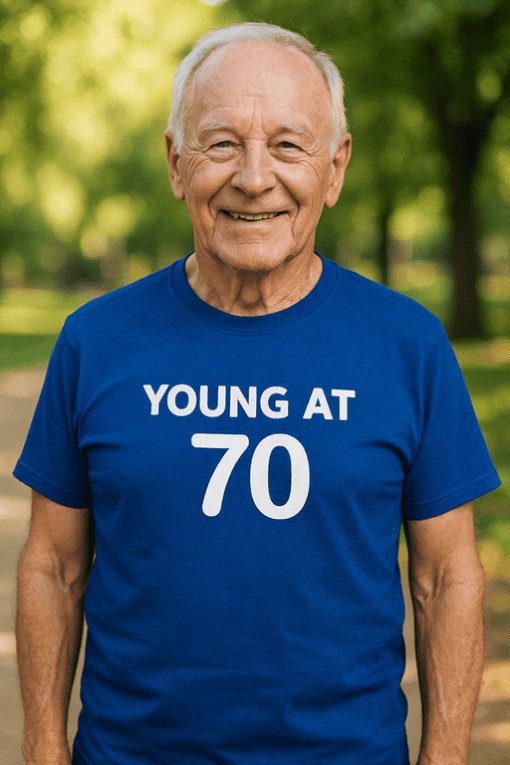 1. Older man smiling wearing a "Young at 70" birthday t-shirt outdoors.