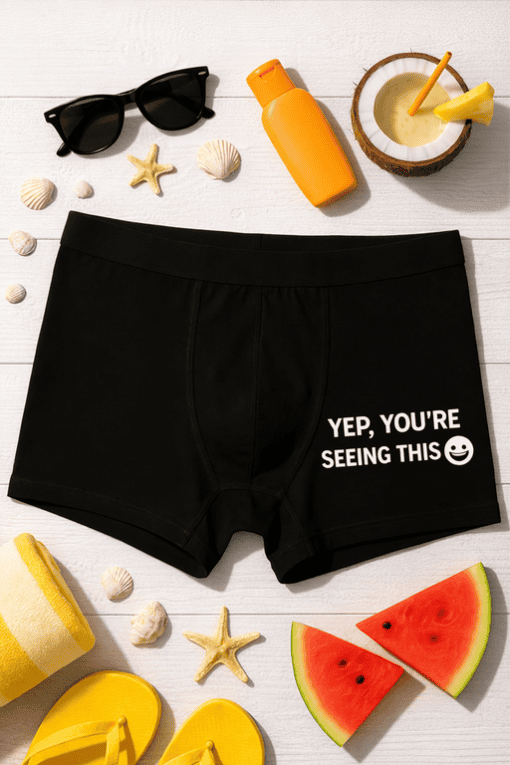 Black boxer briefs with humorous "YEP, YOU'RE SEEING THIS" quote on the front, laid out with summer beach accessories.