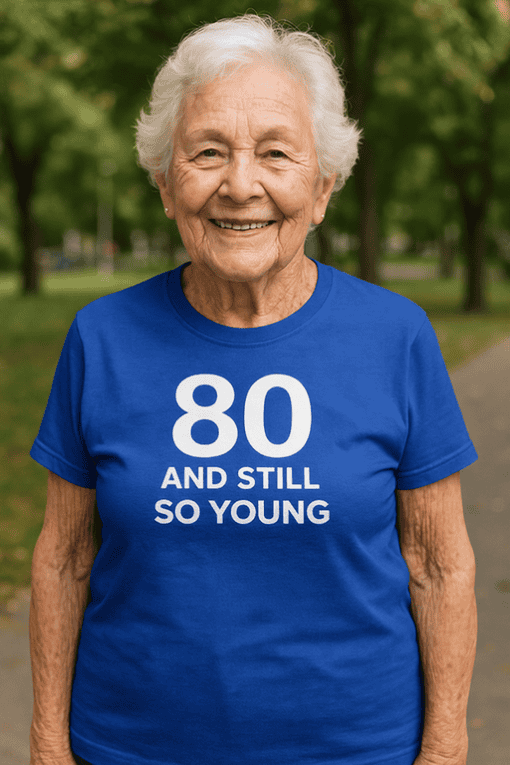 1. Happy elderly woman wearing a blue birthday T-shirt with "80 and still so young" phrase.