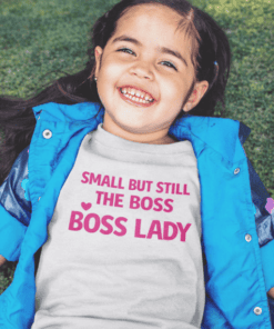 Small girl wearing a T-shirt with "Small but still the boss, boss lady" pink text, outdoor setting.