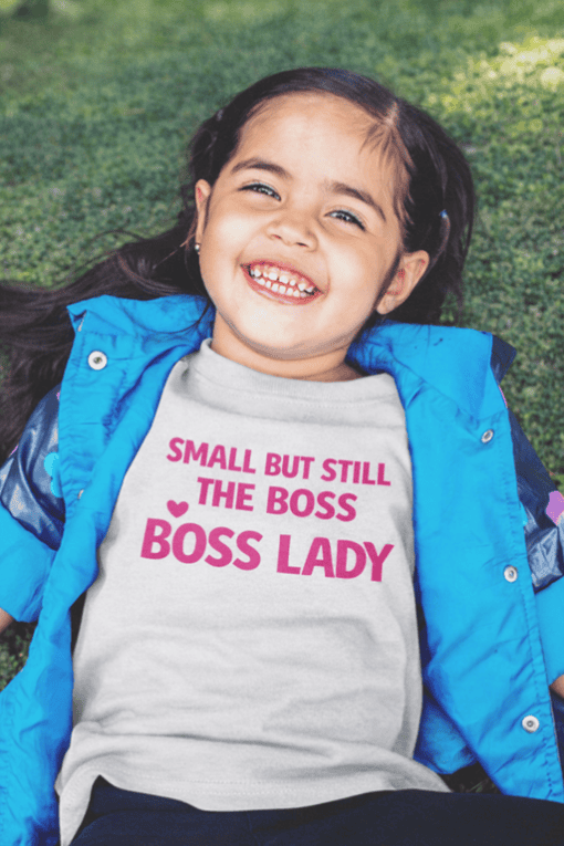Small girl wearing a T-shirt with "Small but still the boss, boss lady" pink text, outdoor setting.