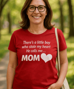 A woman wearing a red T-shirt with a heartfelt mom quote, standing outdoors in a park setting.