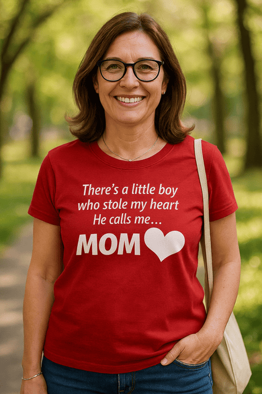 A woman wearing a red T-shirt with a heartfelt mom quote, standing outdoors in a park setting.