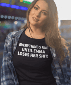 - Woman wearing black T-shirt with humorous text about Emma, casual street style, vibrant nightlife background.