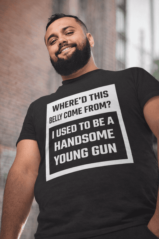 Smiling man wearing humorous handgun print t-shirt, urban background, casual fashion.
