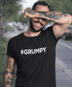 Relaxed man smiling in black "#GRUMPY" T-shirt, casual outdoor setting.
