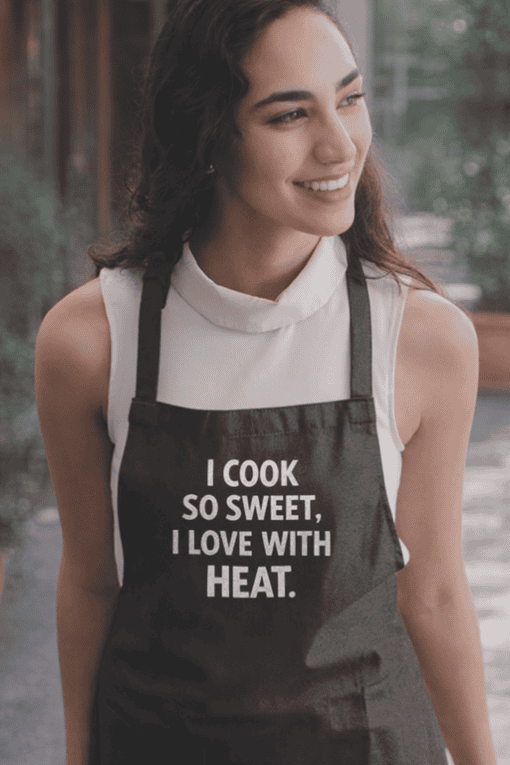 Smiling woman wearing a black apron with humorous cooking quote for kitchen or chef enthusiasts.