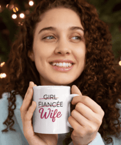 Cute woman with curly hair holding a coffee mug that says "Girl Fiancee Wife" perfect for wedding gifts.