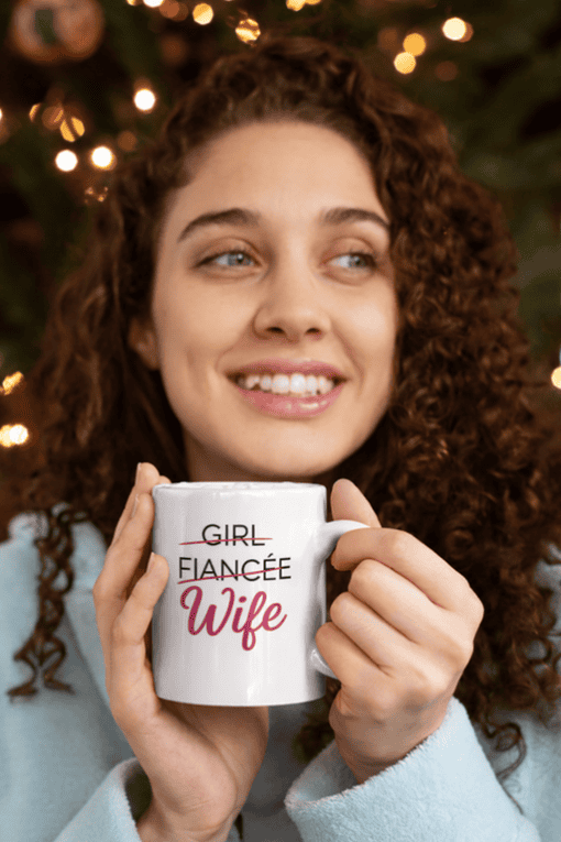 Cute woman with curly hair holding a coffee mug that says "Girl Fiancee Wife" perfect for wedding gifts.