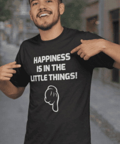 Happy face pointing to tee with "Happiness is in the little things" slogan and animated illustration, casual outdoor setting.