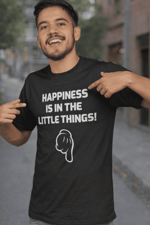 Happy face pointing to tee with "Happiness is in the little things" slogan and animated illustration, casual outdoor setting.