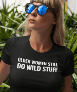 Bold sunglasses woman wearing a black T-shirt with funny quote, outdoor setting.